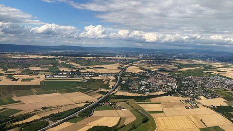 Das BIld zeigt eine Landschaft mit Feldern, Ortschaften und Straßen. Es ist eine Aufnahme aus dem Flugzeug.