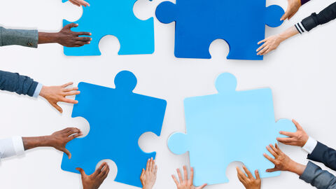 Draufsicht von Menschen die mit ihren Händen vier Puzzleteile aneinanderlegen