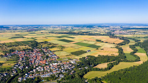 Das Bild zeigt eine Landschaftsaufnahme aus der Luft. Zu sehen sind Felder, Straßen und Dörfer.