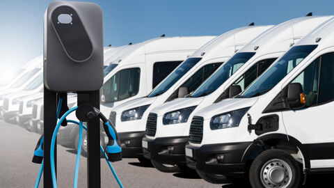 Ladesäule vor einer Flotte von weißen Lieferwagen