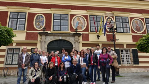 Personengruppe vor beigerotem Gebäude mit Sprossenfenstern
