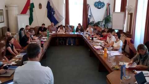 Personen sitzen um u-förmigen Tisch